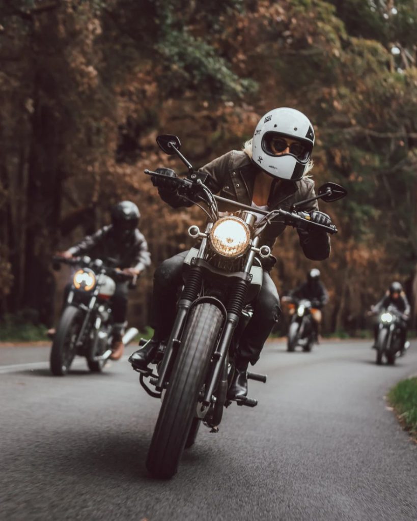 Woman riding Mutt motorcycle leading on a winding country road