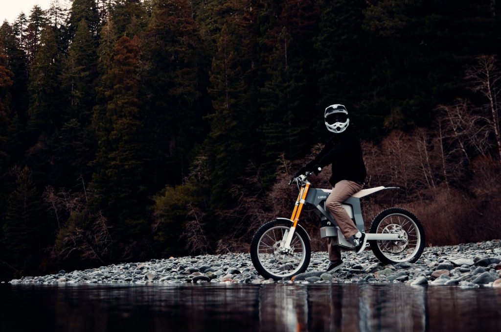 Cake electric motorcycle riding off-road in a natural wilderness setting.