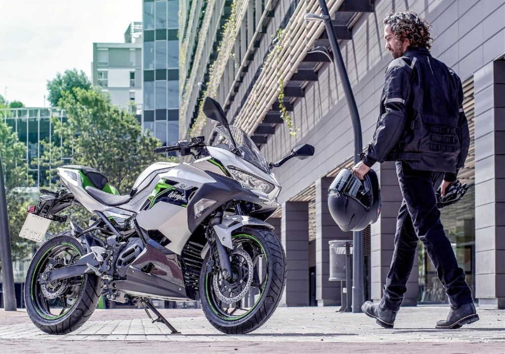 Rider on a Kawasaki Ninja e-1 electric motorcycle riding on city roads.