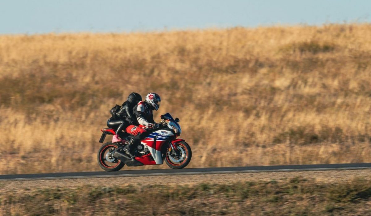a-man-rwith-woman-passenger-riding-a-red-motorcycle-down-a-road-kJfugpeDwL0
