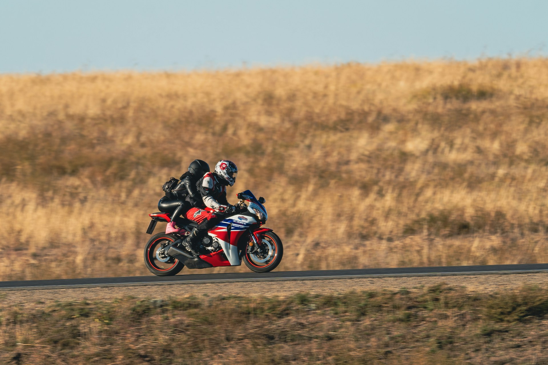 a-man-rwith-woman-passenger-riding-a-red-motorcycle-down-a-road-kJfugpeDwL0